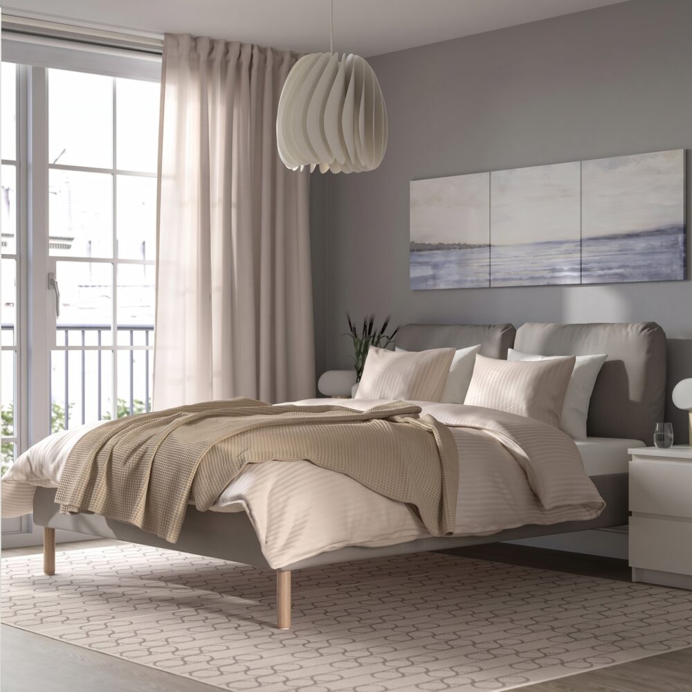 Modern beige upholstered platform bed with a cushioned fabric headboard, wooden legs, and minimalist Scandinavian bedroom design.