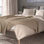 Modern beige upholstered platform bed with a cushioned fabric headboard, wooden legs, and minimalist Scandinavian bedroom design.