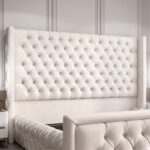 Luxury white upholstered platform bed with diamond-tufted wingback headboard and matching padded footboard in a modern bedroom.