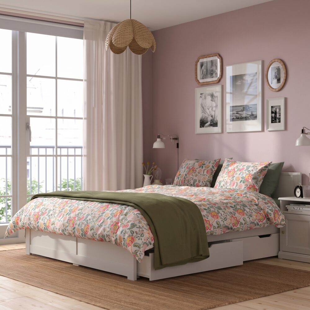 Modern white wooden platform bed with minimalist panel headboard, contemporary bedroom furniture, floral bedding, and clean Scandinavian-inspired design.