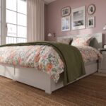 Modern white wooden platform bed with minimalist panel headboard, contemporary bedroom furniture, floral bedding, and clean Scandinavian-inspired design.