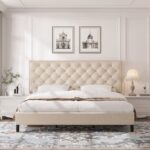 Modern beige upholstered platform bed with button tufted nailhead headboard, low-profile frame, sturdy wooden slats, and elegant contemporary bedroom design.