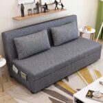 Modern grey fabric sofa cum bed with removable cushions, integrated side storage pockets, and convertible sleeper design in a contemporary living room.
