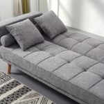 Modern grey fabric convertible sofa bed with tufted backrest, wooden legs, square cushions, bolster pillows, and Scandinavian design for living room furniture.