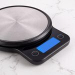 Homslux digital kitchen scale with brushed stainless steel circular platform on a white marble countertop