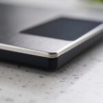 Homslux stainless steel digital kitchen scale with a large black display screen on a white speckled countertop next to fresh vegetables
