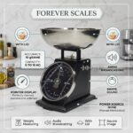 Homslux matte black vintage mechanical kitchen scale with stainless steel bowl on a wooden rustic table next to a bowl of red apples