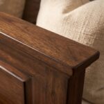 Dark walnut brown single bed with a classic paneled wooden headboard and footboard, styled with cream bedding and a textured beige throw in a cozy bedroom.
