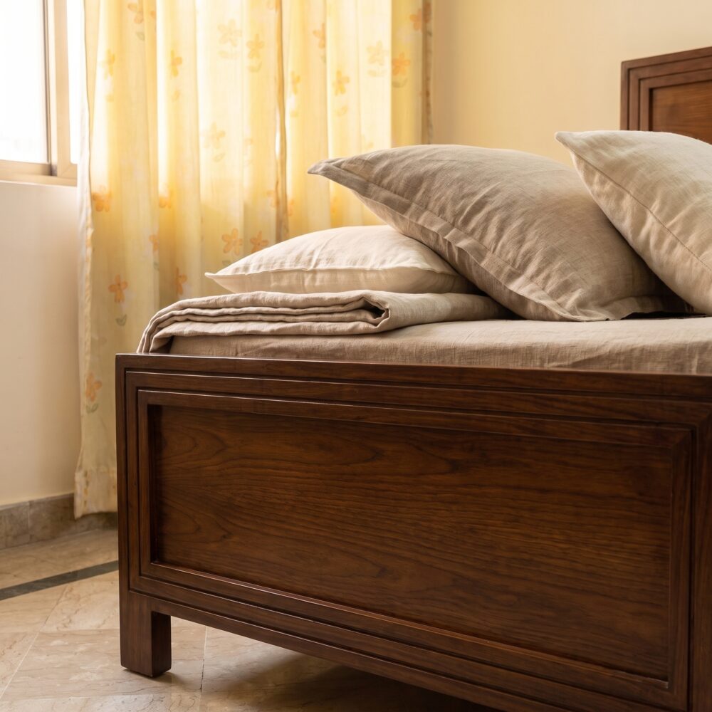Dark walnut brown single bed with a framed rectangular panel headboard, raised wooden-style legs, cream bedding, knitted beige throw, and neutral bedroom décor.