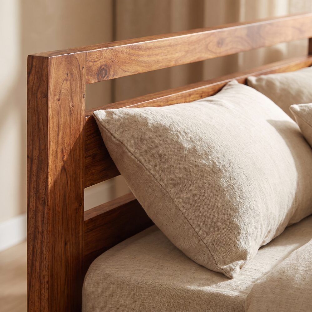Solid natural wood single bed frame with an open horizontal slatted headboard styled with cozy beige linen bedding and a chunky knit throw blanket.