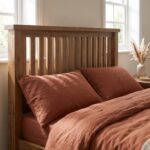 Rustic solid oak wood single bed frame featuring a vertical slatted headboard styled with beige linen bedding next to a matching oak nightstand.